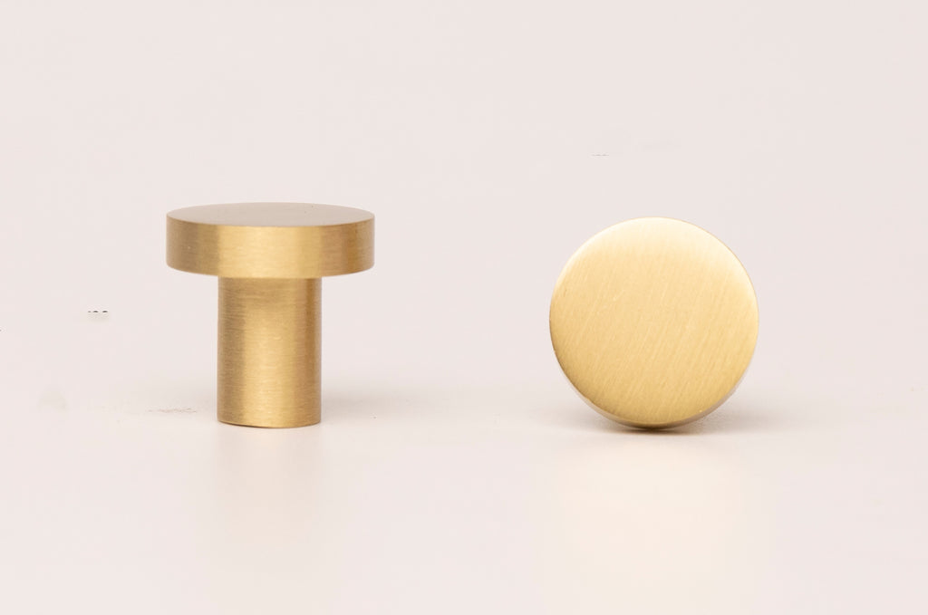 The image showcases two identical, circular brass knobs with protruding handles on a white background. The knobs are polished and reflect the surrounding light, highlighting the intricate details of the brass material. The composition focuses solely on the knobs, providing no context about their intended use or location.